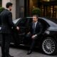 Professional chauffeur opening the door of a luxury executive sedan for a VIP business client outside a premium corporate building.