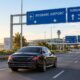Luxury chauffeur car beneath Brisbane Airport and Sunshine Coast directional signs