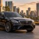 Black luxury chauffeur sedan outside a modern building with a city skyline at sunset.
